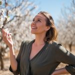 Woman in a blooming almond orchard with radiant, nourished skin, symbolizing the gentle moisturizing and soothing benefits of sweet almond oil in skincare.