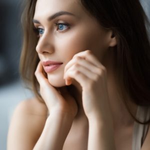 Woman with naturally radiant, hydrated skin gazing softly by a window, representing gentle, botanical skincare and a calm daily skincare ritual.
