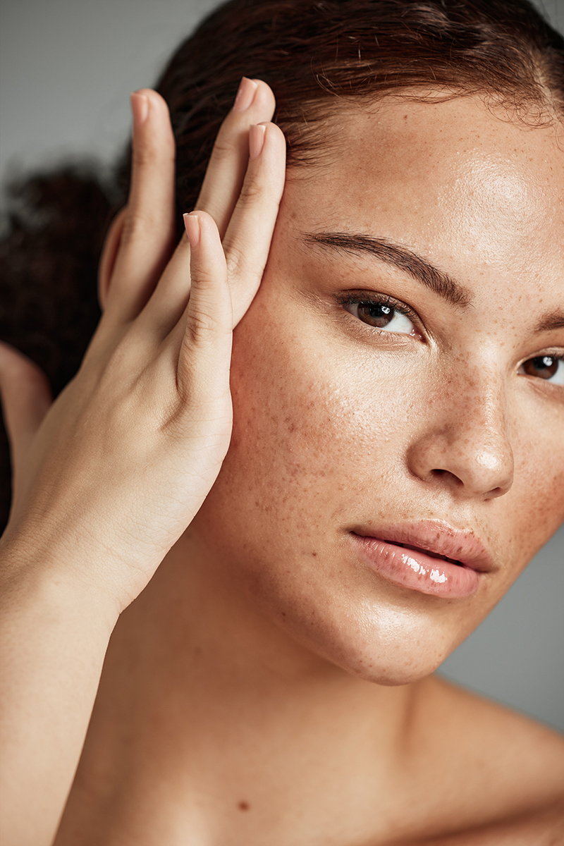 Woman with natural freckles and radiant skin touching her face, showcasing ORY Skincare botanical infusion formulas designed for every skin type.