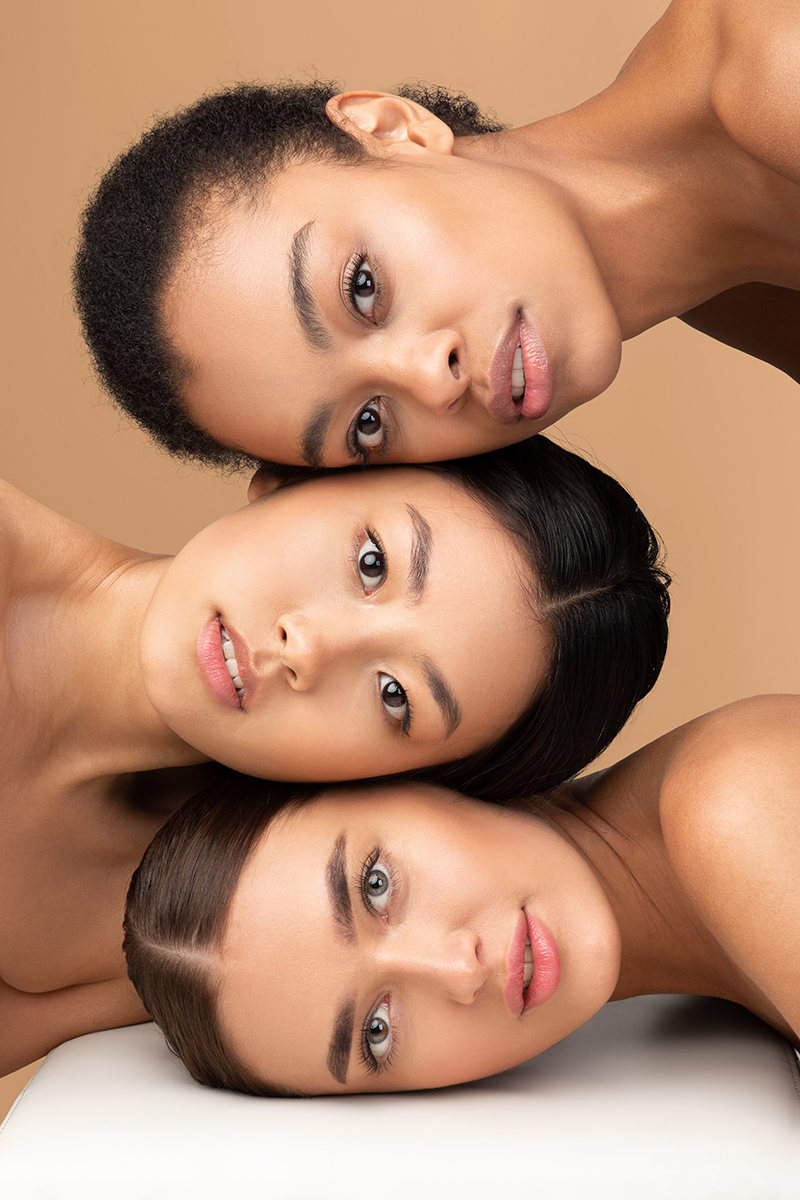Three women with different skin tones rest their heads together, showcasing smooth, healthy skin that represents ORY Skincare’s botanical infusion solutions for every skin type.