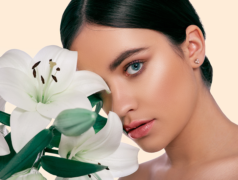 Woman with luminous skin holding a white lily, symbolizing ORY Skincare’s botanical-infused philosophy and commitment to natural beauty.