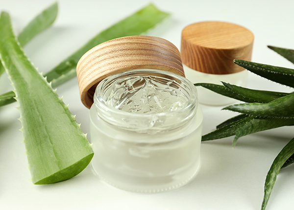Glass jar of aloe vera and tea tree gel surrounded by fresh aloe leaves, showcasing a calming, botanical skincare ingredient by ORY Skincare.