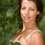 Woman with clear, balanced skin standing among green leaves, representing Witch Hazel Extract used in ORY Skincare for soothing, toning, and refining pores.