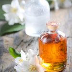 Glass bottles of amber jasmine infused oil and clear essence with fresh white jasmine flowers on wooden surface, illustrating the luxurious Jasmine Infused Oil in Oryskincare's nourishing skincare products for hydrated, anti-aging skin benefits.