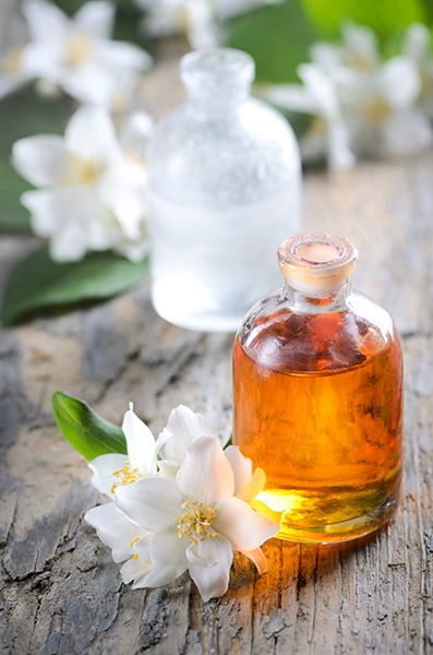 jasmine_infused_oil Glass bottles of amber jasmine infused oil and clear essence with fresh white jasmine flowers on wooden surface, illustrating the luxurious Jasmine Infused Oil in Oryskincare's nourishing skincare products for hydrated, anti-aging skin benefits.
