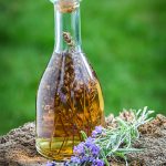 Glass bottle of golden lavender-infused oil with lavender sprigs inside, placed outdoors on a rustic wooden surface for ORY Skincare’s Lavender Oil Infusion ingredient.