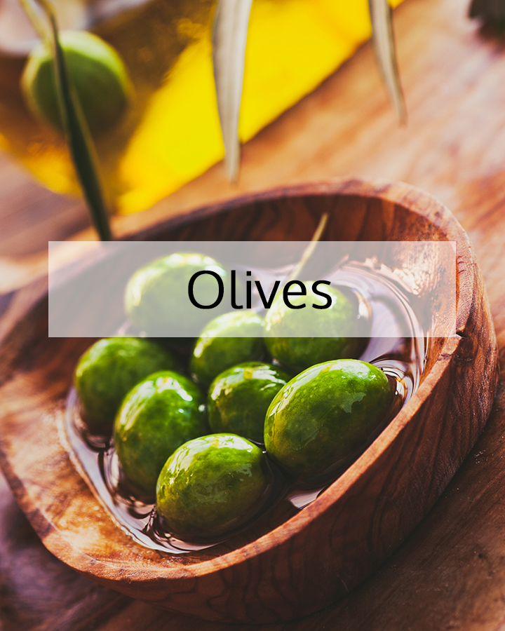 Fresh green olives resting in a wooden bowl with olive oil, representing ORY Skincare’s use of olives as a nourishing botanical ingredient rich in antioxidants and skin-protective lipids.