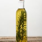Rosemary infused oil in a clear glass bottle, showcasing fresh rosemary sprigs suspended in golden botanical oil for natural skincare formulation.