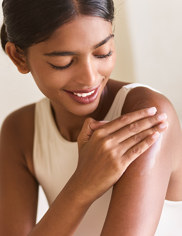 Woman gently applying moisturizing cream to her shoulder during a skincare routine, showcasing smooth, hydrated skin with ORY Skincare.