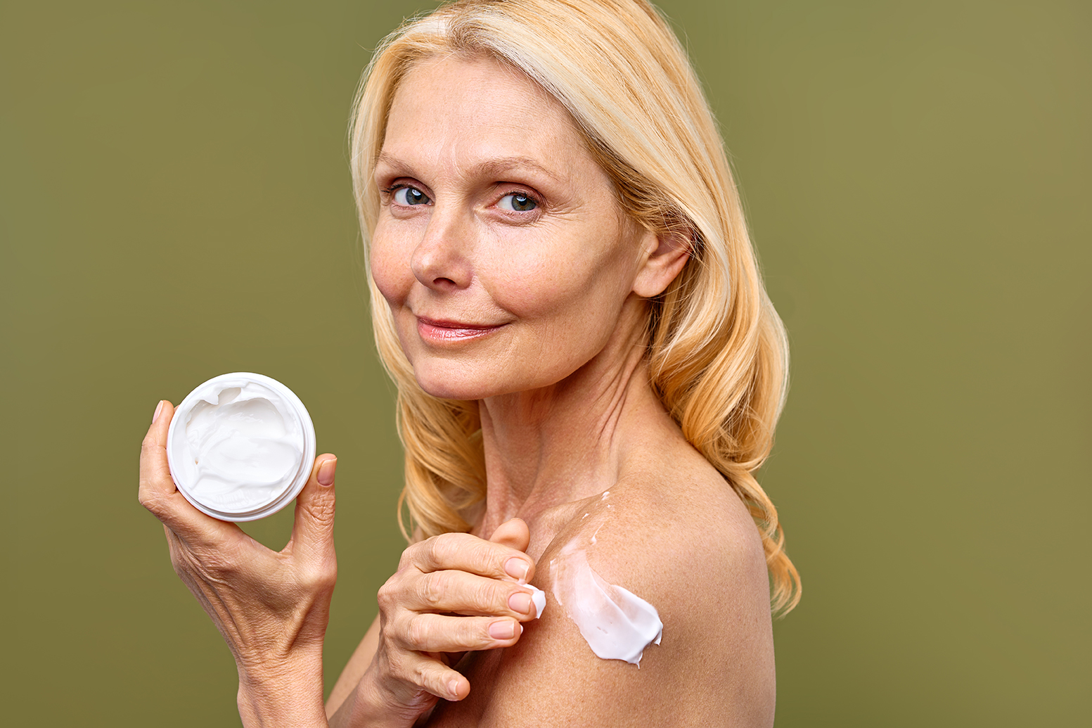 Smiling mature woman applying moisturizing cream to shoulder, showcasing healthy radiant skin for ORY Skincare mature skincare.
