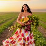Woman in floral dress walking through sunny field holding fresh sugarcane, corn, and beets, symbolizing natural plant-derived Lactic Acid in Oryskincare's gentle exfoliating products for smoother, brighter skin.