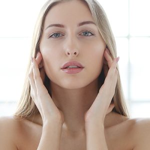 Woman with calm, clear complexion gently touching her face, showcasing ORY Skincare’s soothing serum for sensitive skin.
