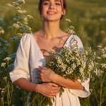 Woman holding fresh feverfew flowers in a sunlit field, representing the calming and anti-inflammatory benefits of Feverfew Extract in ORY Skincare.