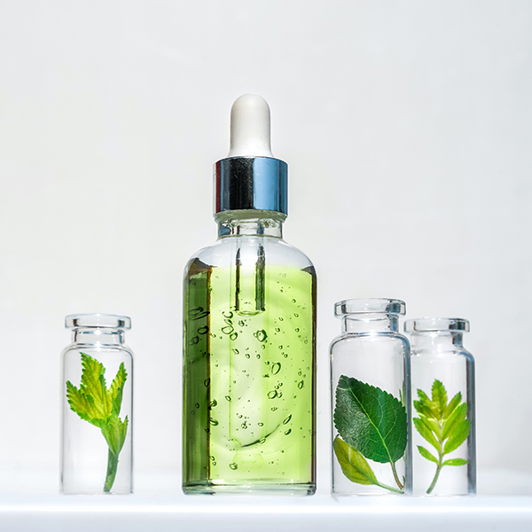 Bi-phasic infusion cosmetic serum with botanical leaves and visible oil and water phases, representing natural skincare and haircare made with homeopathic vegetable oils.