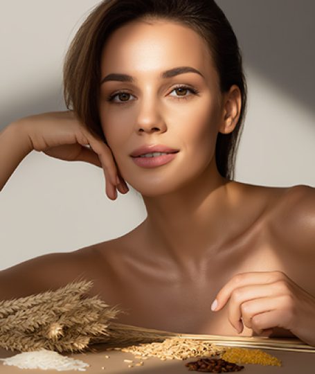 Woman with radiant skin beside natural grains representing Ferulic Acid antioxidant benefits in ORY Skincare formulations.