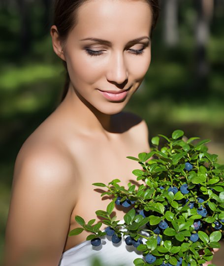 Woman holding fresh wild bilberries and green leaves outdoors, representing wild bilberry extract used in ORY Skincare for antioxidant and skin-brightening benefits.