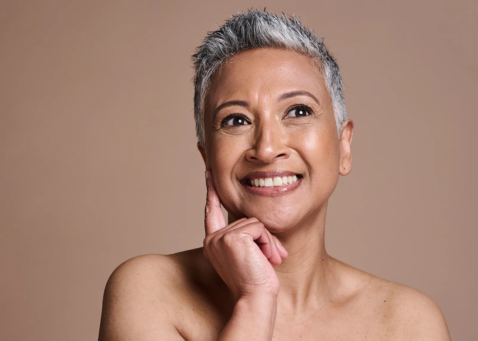 Smiling mature woman with radiant, healthy skin touching her face — ORY Skincare mature skincare for hydration, firmness, and radiance.